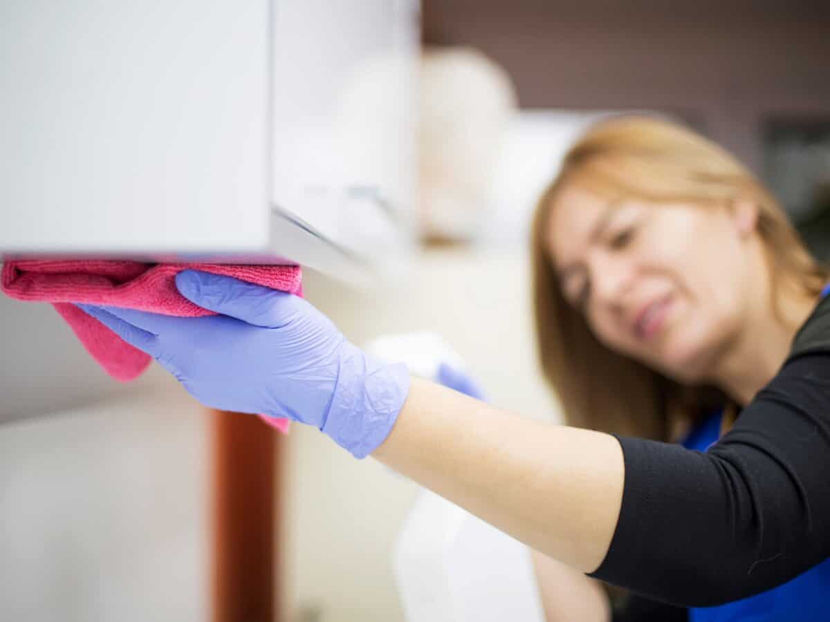 Een medewerker poetst een keukenkastje.